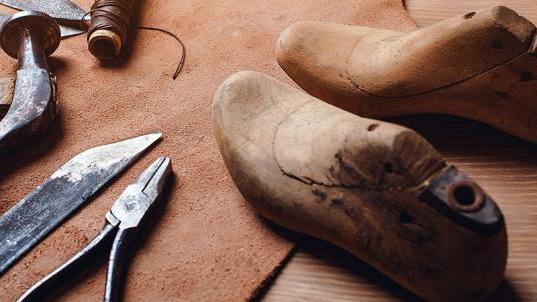 Wooden shoe lasts stand on a piece of leather with various tools next to them